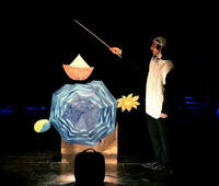 Immagine dello spettacolo: attore-pinguino, ombrello e bagaglio